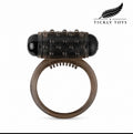 An adult novelty device featuring a translucent dark brown silicone ring with a textured black studded cylinder on top, shown against a plain white background with the Tickly Toys brand logo in the top right corner.